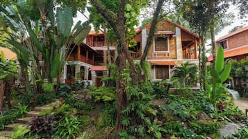 A traditional house with a red roof, surrounded by lush greenery and a variety of plants.