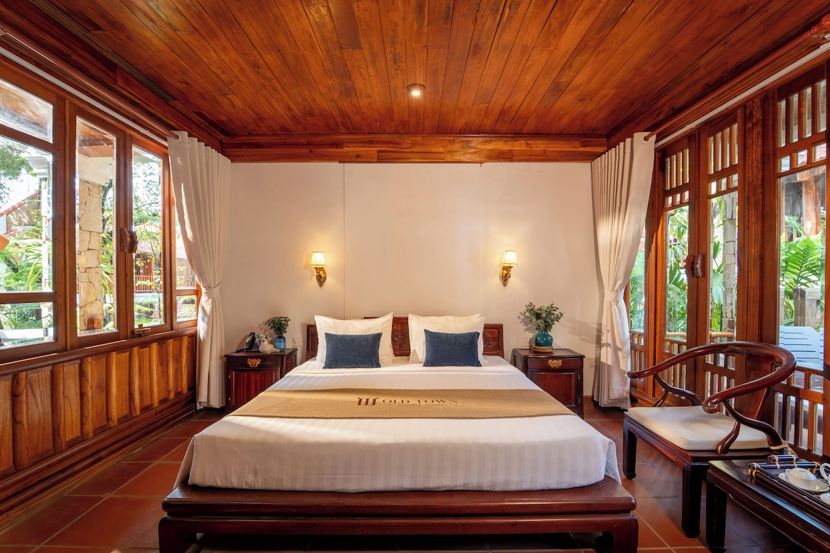 A large bed with a wooden headboard, two bedside tables with lamps, and a chair with a tray.
