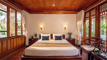 A large bed with a wooden headboard, two bedside tables with lamps, and a chair with a tray.