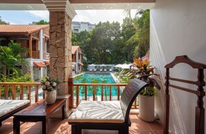 A balcony with a view of a swimming pool, a wooden chair, a bench, and a potted plant. - Old Town Boutique Resort (Phu Quoc)