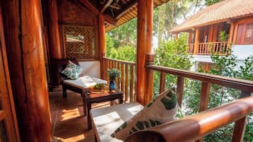 A wooden balcony with a cushioned seating area, a small table with a fruit bowl, and a potted plant.