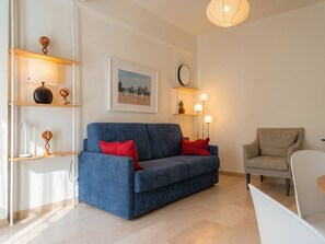 A modern living room with a blue sofa, red cushions, a white armchair, and a dining table. There are shelves with decorative items and a framed picture on the wall. - Versilia Escape Seaside Retreat (Camaiore)