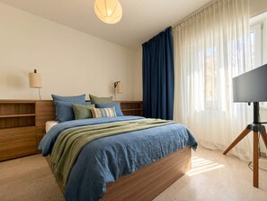 A bedroom with a bed, bedside tables, a lamp, curtains, and a TV on a tripod. - Versilia Escape Seaside Retreat (Camaiore)