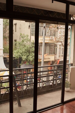 A view through a window with a metal railing, a street scene with buildings, and a tree. - Central Old Quarter: City View Balcony, Walk to Night Market (Hà Nội)