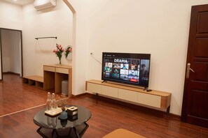 A living room with a flat-screen TV on a wooden stand, a small round table with decorative items, and a door to the right. - Central Old Quarter: City View Balcony, Walk to Night Market (Hà Nội)