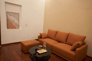 Een woonkamer met een bruine bank, een klein rond tafeltje met een dienblad, en een lijstwerk aan de muur.