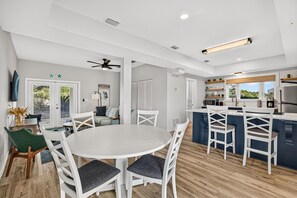 Une cuisine moderne avec des meubles blancs, un îlot central et un coin repas comprenant une table ronde et des chaises.