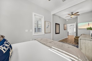 A bedroom with a bed, a ceiling fan, a window with blinds, and a painting on the wall. - Steps to the Beach | Sleeps 13 | 2 Living Spaces (Port St Joe)