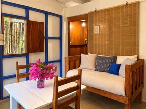 Ein Zimmer mit einer Holzsofa, einem Esstisch mit Stühlen und einer Wand mit Bambusrollos.