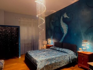 A bedroom with a bed, a wall mural, a chandelier, and a nightstand. - SOGNI SUL MARE 5 TERRE-JRE (La Spezia)