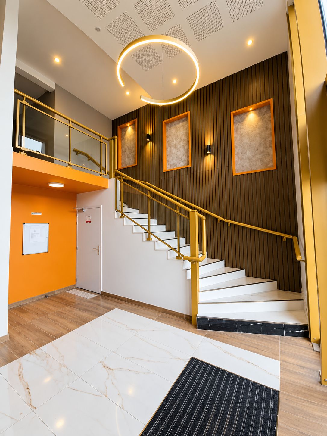 A modern interior with a staircase, a reception desk, and a ceiling with a circular light fixture.