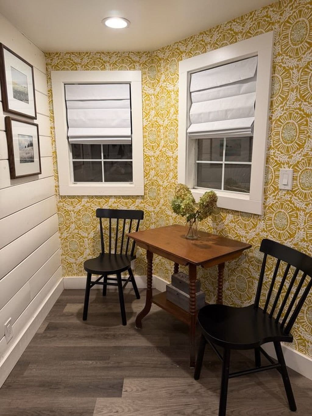 A corner room with two windows, a wooden table, and two chairs.
