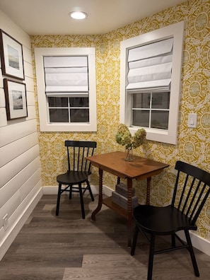 A corner room with two windows, a wooden table, and two chairs. - Cozy Cottage on a Working Flower Farm — Private Deck, Fire Pit, Near Sacramento (Loomis)