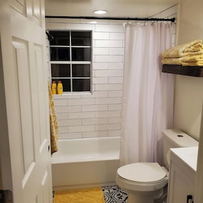 A bathroom with a white bathtub, a toilet, and a window with a curtain. - Cozy Cottage on a Working Flower Farm — Private Deck, Fire Pit, Near Sacramento (Loomis)