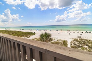 Ein Strand mit blauem Himmel, einer Holzterrasse und einem sandigen Ufer mit Sonnenschirmen und Liegestühlen.
