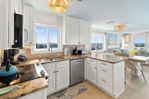 A modern kitchen with white cabinetry, a granite countertop, and a view of the ocean through large windows. - Palapa House • Gulf Front • Palapa + Hammock • Sleeps 11 (Panama City Beach)