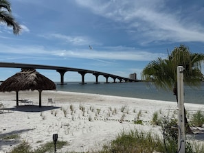 Ein Strand mit einem Strohdachschirm, einer Palme und einer Brücke im Hintergrund.