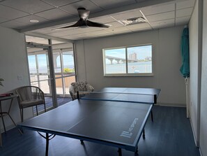 Ein Zimmer mit einem Tischtennis-Tisch, einem Deckenventilator, einem Fenster mit Blick auf eine Brücke und einem Sessel.