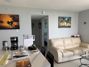 Ein Wohnzimmer mit einem beigefarbenen Ledersofa, einem Glastisch und einem Essbereich mit einem weißen Tisch und Stühlen.