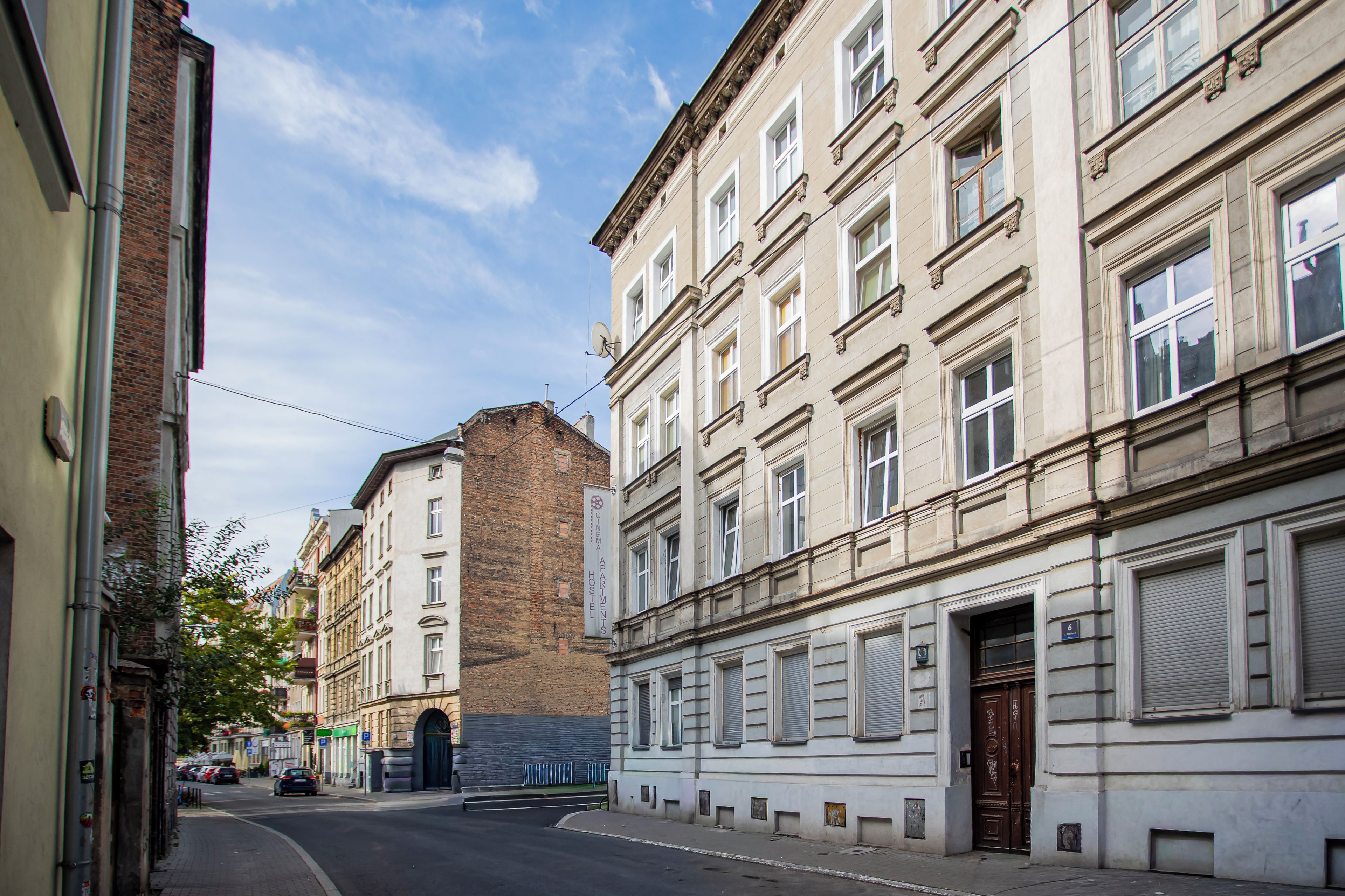Vista de calle con edificios, incluyendo una construcción de ladrillo y un edificio blanco con un cartel que dice 'Cinema Apartments Hostels'.