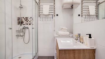 Un baño moderno con cabina de ducha de vidrio, un lavabo blanco con artículos de aseo y un mueble de tocador de madera.
