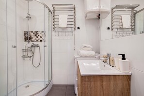 A modern bathroom with a glass shower enclosure, a white sink with toiletries, and a wooden vanity. - Klimatyczny Apartament Strzałowa  (Poznań)