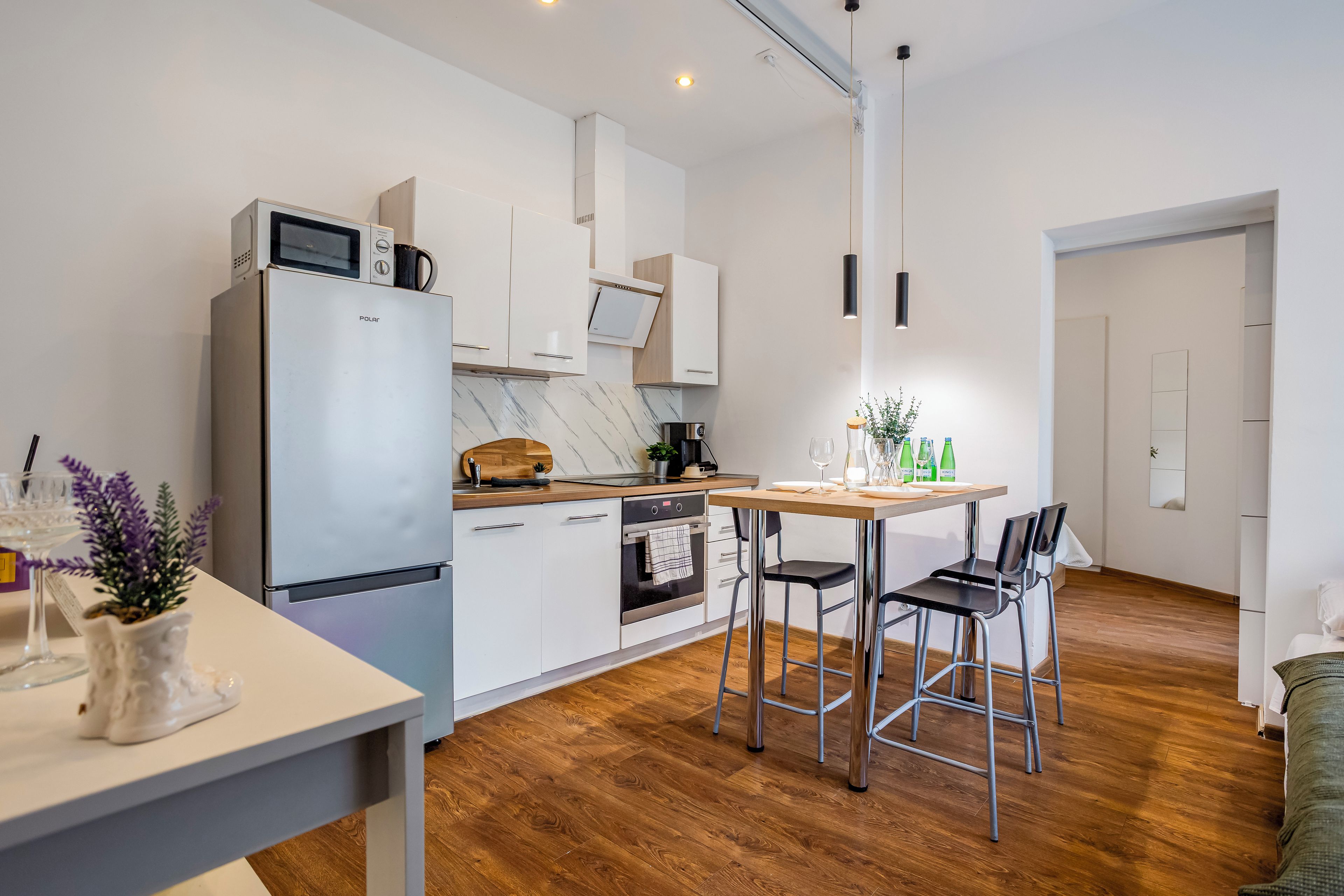 Una cocina moderna con refrigerador, microondas y horno. Hay una mesa de comedor con sillas y una pequeña planta en maceta.