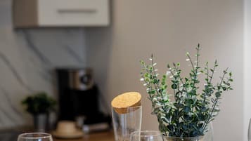 Una mesa de comedor con platos blancos, un florero de vidrio con follaje verde y una jarra de vidrio con tapón de corcho.