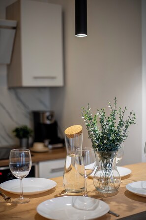 A dining table with white plates, a glass vase with green foliage, and a glass decanter with a cork stopper. - Klimatyczny Apartament Strzałowa  (Poznań)