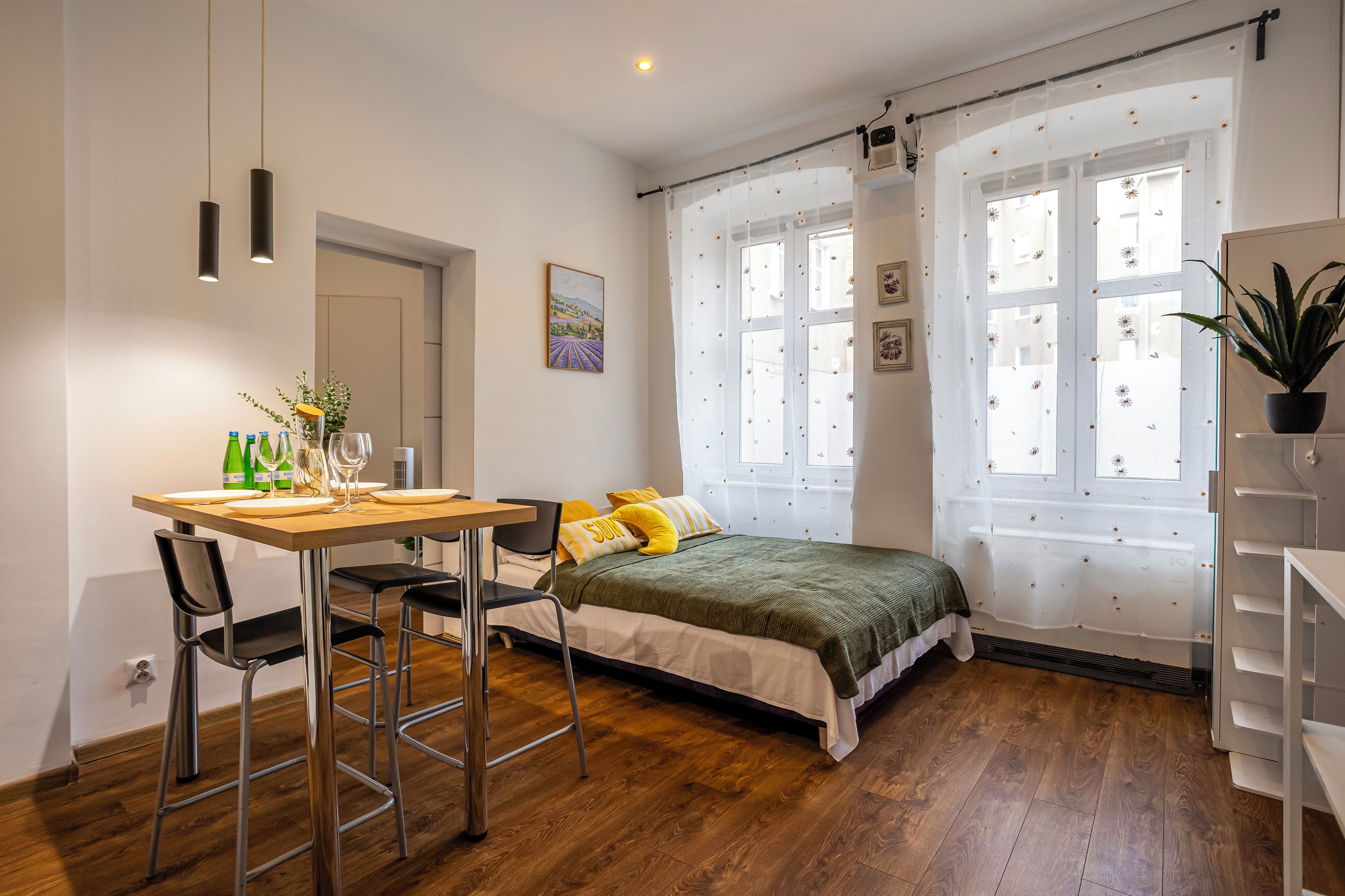 Un dormitorio con cama, un escritorio con sillas, una ventana con cortinas y una planta en maceta.