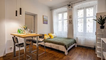 Un dormitorio con cama, un escritorio con sillas, una ventana con cortinas y una planta en maceta.
