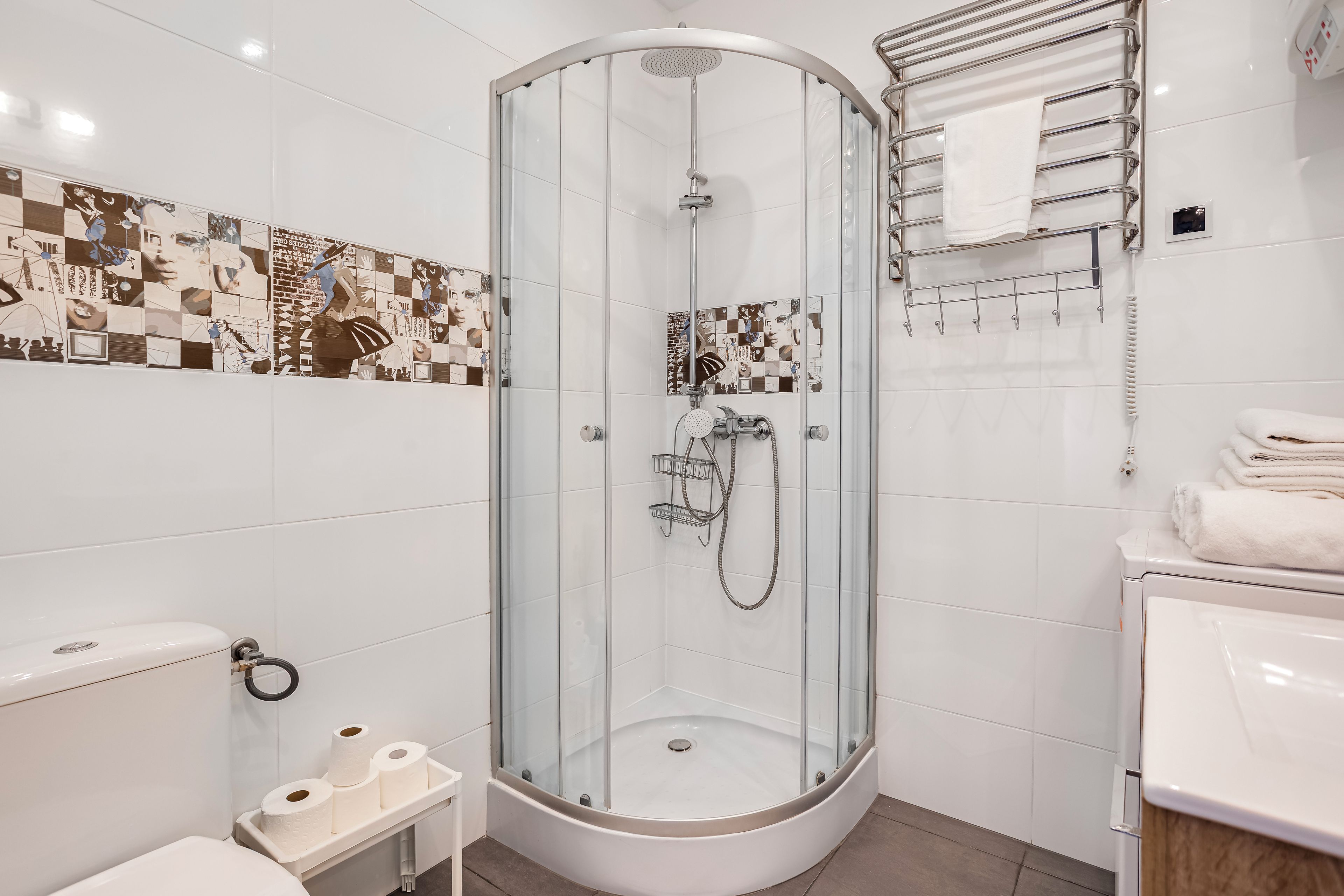 Un baño moderno con ducha envuelta en vidrio, azulejos blancos, inodoro y lavamanos.