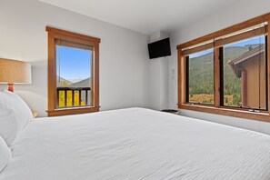 A bedroom with a large bed, two windows with wooden frames, a wall-mounted TV, and a lamp on the left. - Slopeside Luxury at Red Hawk Lodge – Walk to Keystone Gondola (Keystone)