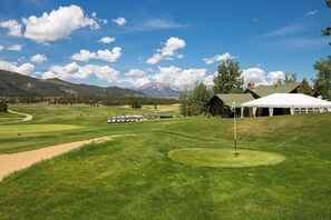 Camp de golf amb una tenda, un edifici i muntanyes al fons.