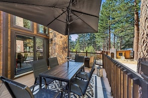 An outdoor patio with a table and chairs, a stone wall, and a view of a forest. - Lake & Après Chalet BBQ, Games, Pool Table (South Lake Tahoe)