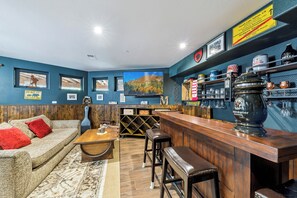 Un espace bar avec des meubles en bois, un téléviseur, ainsi que diverses bouteilles et verres disposés sur des étagères.