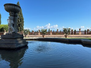 A fountain with a statue, surrounded by a pool, with a clear sky and distant mountains. - Le Falene Guest House (Comeana)