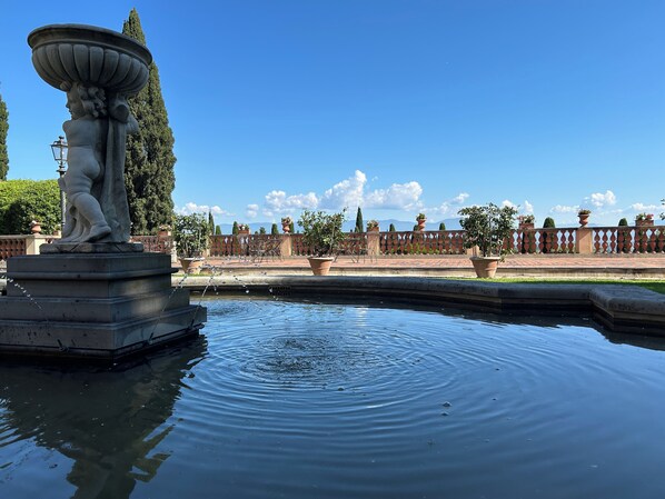 Una fuente con una estatua, rodeada por una piscina, con cielo despejado y montañas a lo lejos.