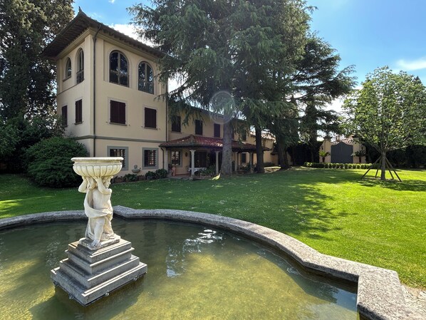 A building with a fountain in front, surrounded by a well-maintained lawn and trees. - Le Falene Guest House (Comeana)