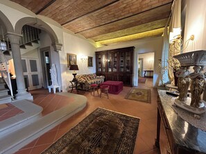 A spacious living area with a high ceiling, a staircase, and a view into another room. - Le Falene Guest House (Comeana)