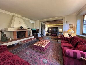 A spacious living room with a fireplace, red sofas, a patterned rug, and a television. - Le Falene Guest House (Comeana)