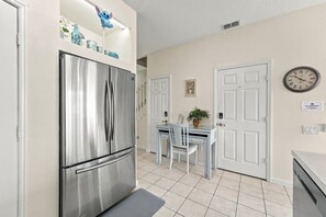 A compact kitchen with a stainless steel refrigerator, a dining table with chairs, and a wall clock. - 3BR/3BA Kissimmee Townhome, Private Pool, Near Disney (Kissimmee)