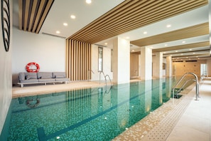 Ein moderner Innenpool mit klarem Wasser, eine Lounge mit einer Couch und ein Rettungsring an der Wand.