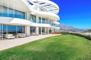 Ein modernes Haus mit einem gebogenen Balkon, einem gepflegten Rasen und Bergblick im Hintergrund.