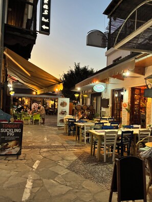 An outdoor dining area with tables and chairs, a sign for a restaurant, and a sign for a pizza place. - 🏡 Modern & Charming spacious 2 bedroom apartment in popular Polis Gardens (Poli Chrysochous)