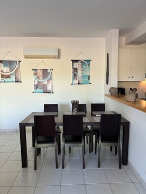 A dining area with a rectangular table and six chairs, a kitchen with cabinets and a countertop, and three abstract wall art pieces. - 🏡 Modern & Charming spacious 2 bedroom apartment in popular Polis Gardens (Poli Chrysochous)