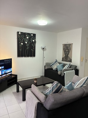 A living room with a black sofa, a coffee table, a TV on a stand, and artwork on the walls. - 🏡 Modern & Charming spacious 2 bedroom apartment in popular Polis Gardens (Poli Chrysochous)