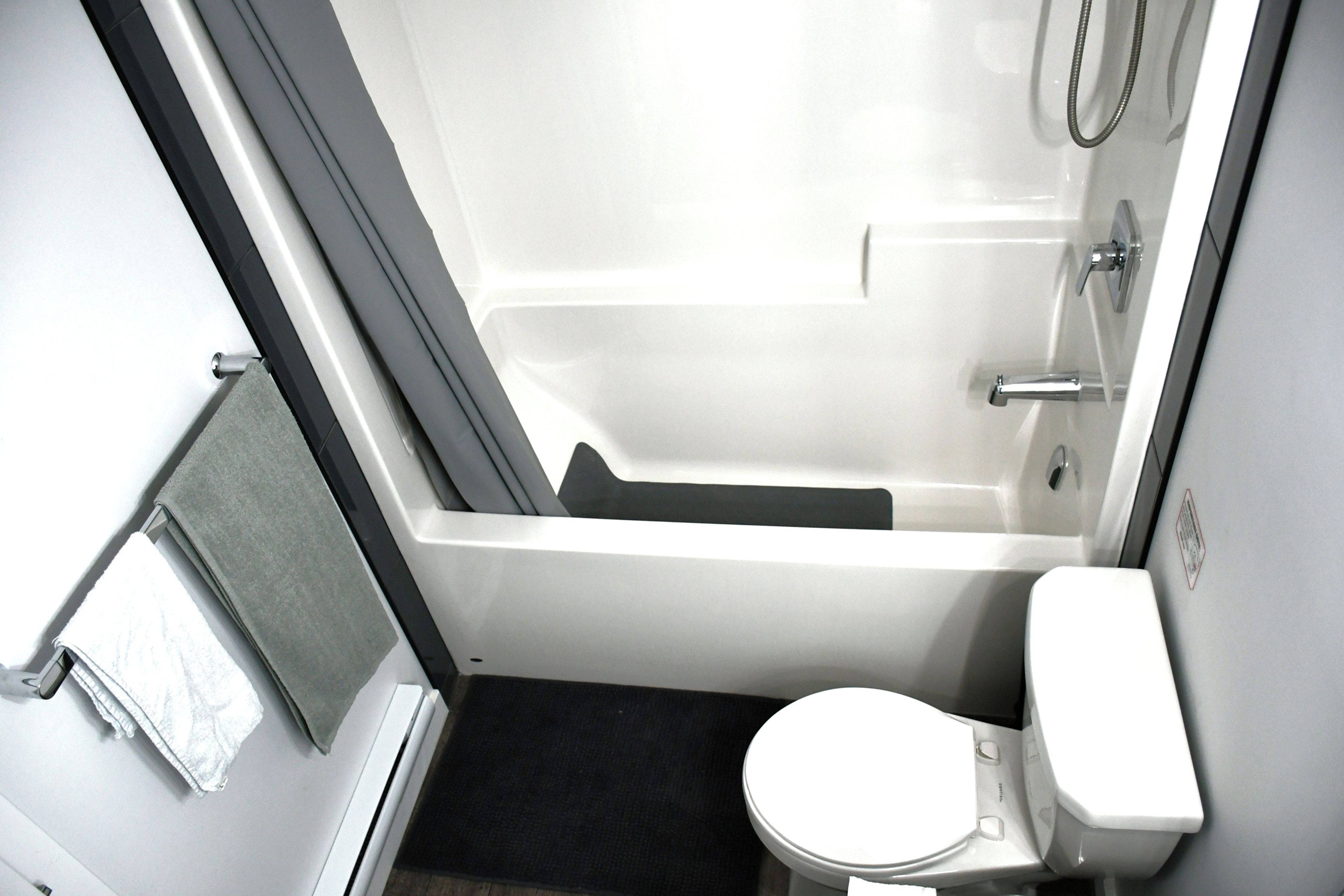 Une petite salle de bain compacte, avec des toilettes blanches, une baignoire et une douche.