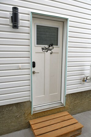 A white door with a 'Welcome' sign, a mailbox, and a small wooden bench outside.