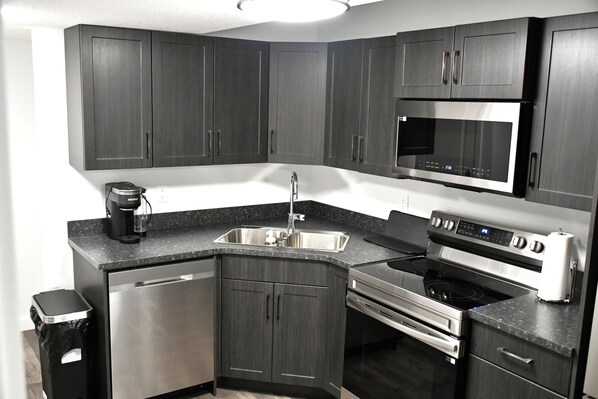 A modern kitchen with dark cabinetry, stainless steel appliances, a dishwasher, and a microwave.